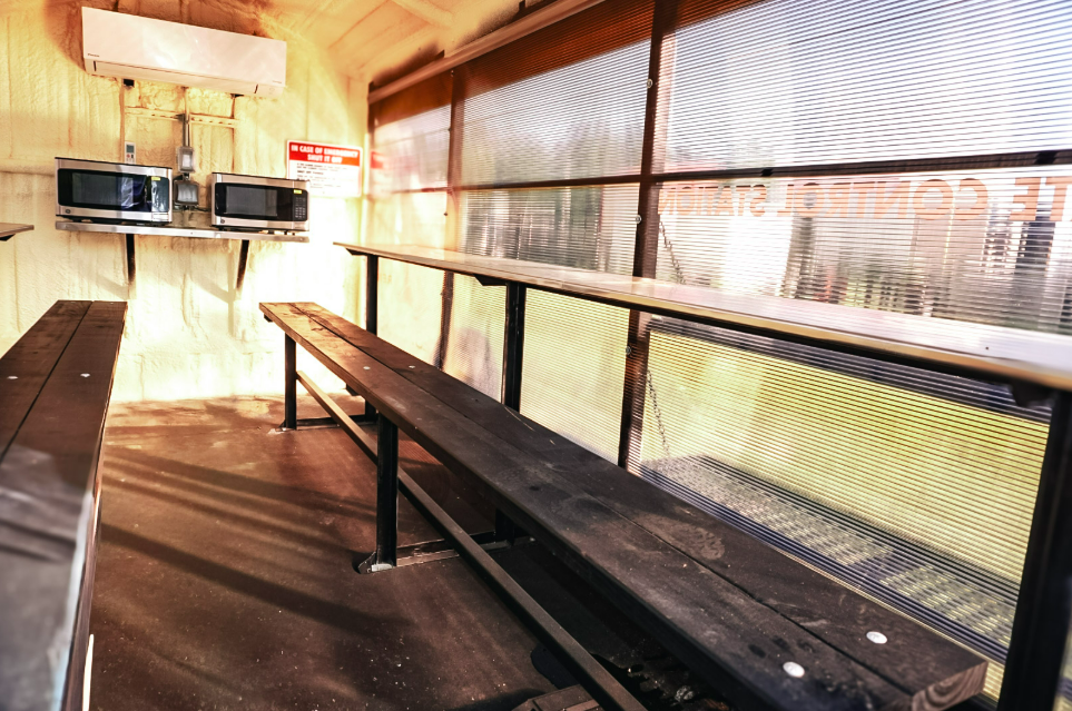 Interior of an Anvil Rentals lunchroom trailer with bar-style bench seating, tables, two microwaves, and a wall-mounted air conditioning head